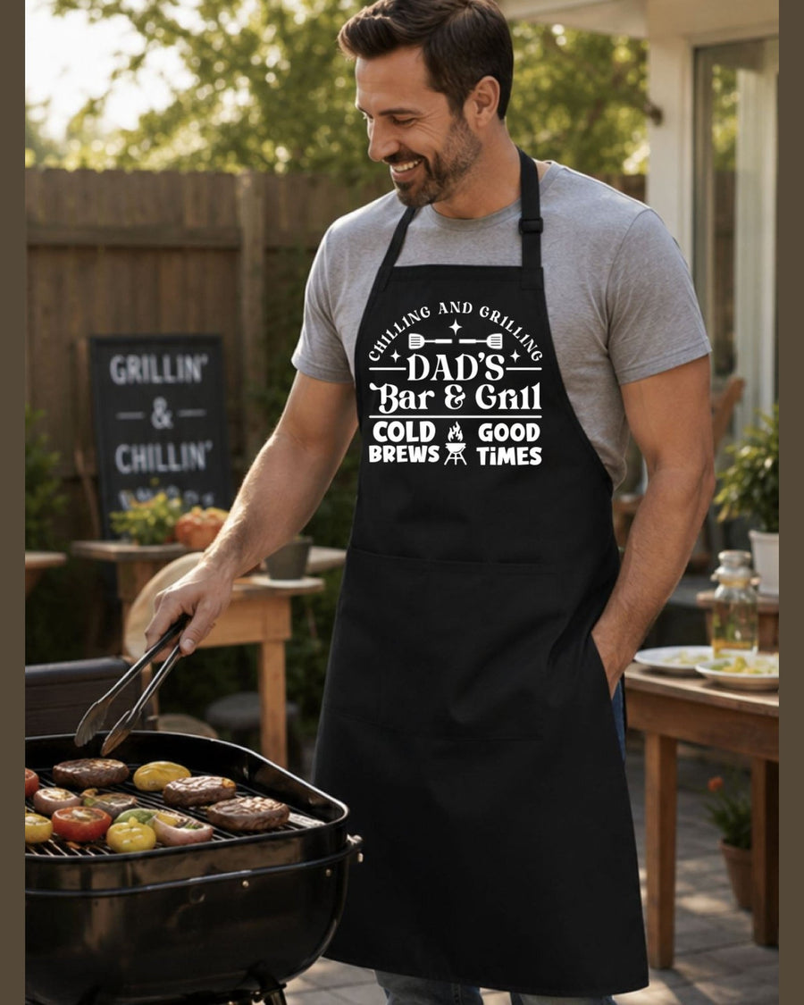 Dad's Bar & Grill BBQ apron with Chilling and Grilling text worn by man cooking burgers outdoors