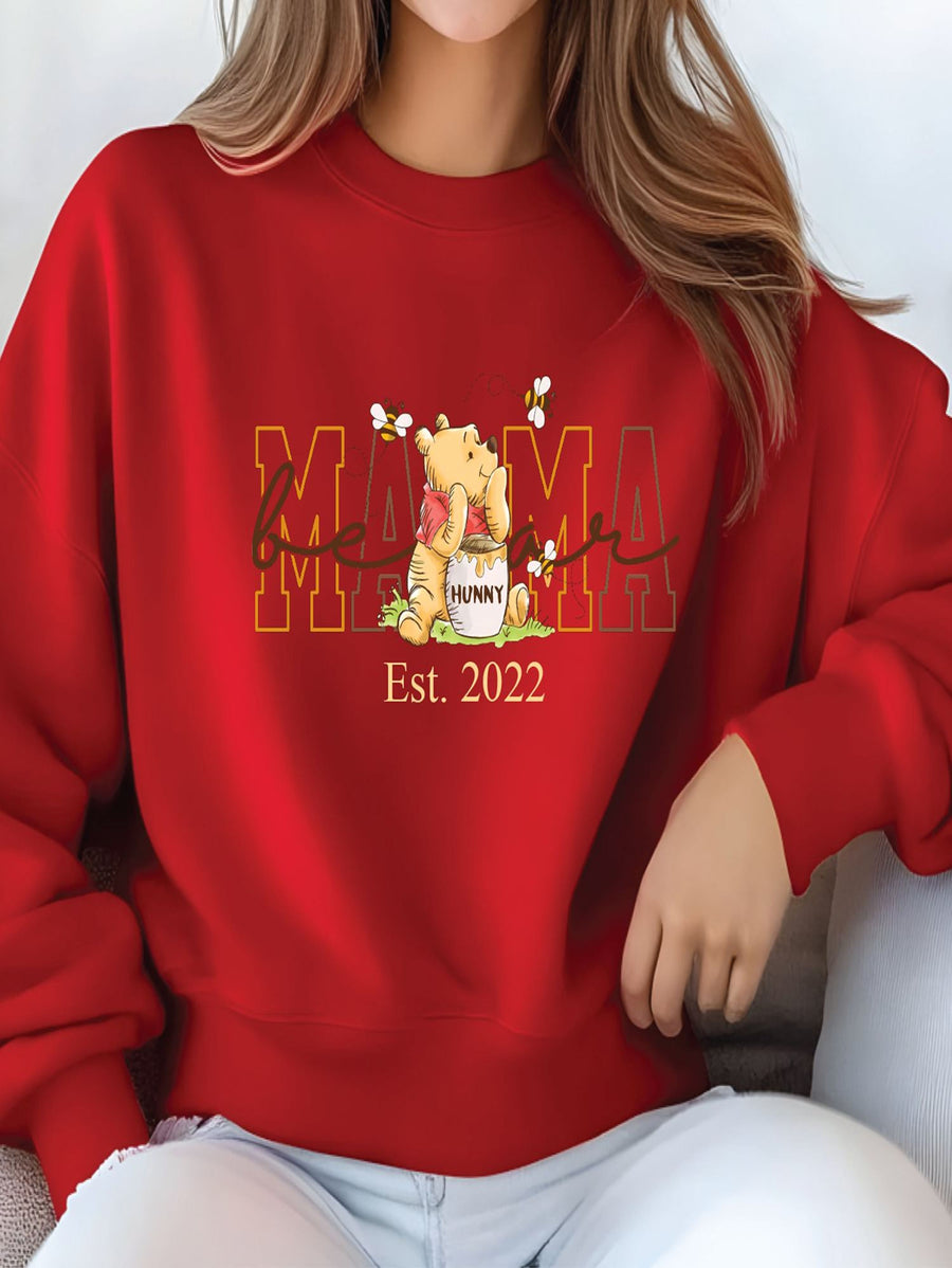 A woman wearing a red sweatshirt with a Winnie the Pooh graphic and text that says "Mama" and "Est. 2022".