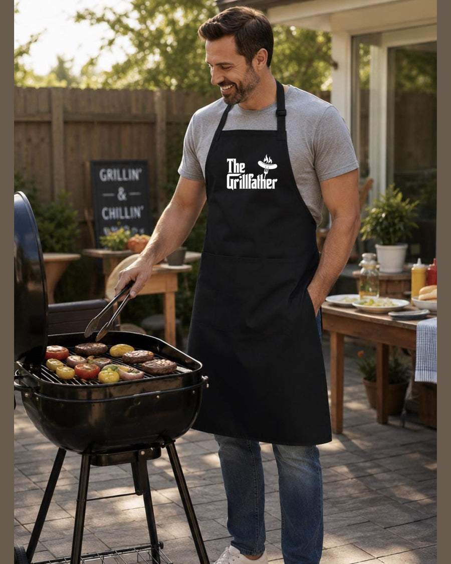 Grill master wearing black The Grillfather apron while cooking meats on kettle grill