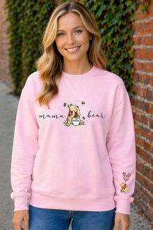 A smiling woman wearing a pink sweatshirt with a Winnie the Pooh design and the text "mama bear" printed on it.