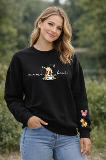 A smiling woman wearing a black sweatshirt with a Winnie the Pooh design and text printed on it, standing in a natural outdoor setting.