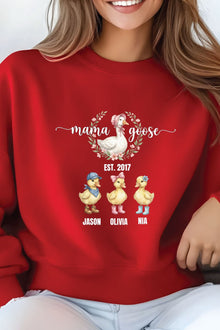 A woman wearing a red sweater with a graphic design featuring three cartoon ducks and the text "mama goose" above them.