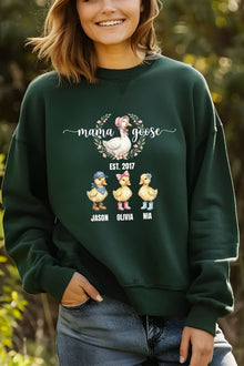 A woman wearing a green sweatshirt with a graphic design featuring three cartoon ducks and the text "mama goose" above them.