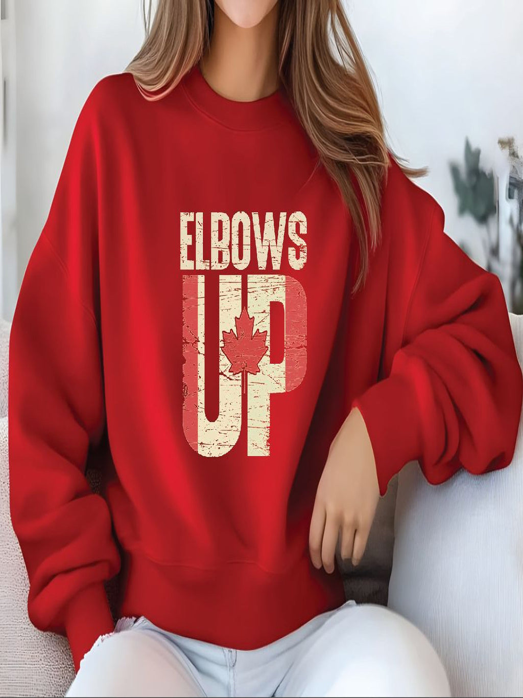 A woman wearing a red sweatshirt with the text "ELBOWS UP" printed on it.