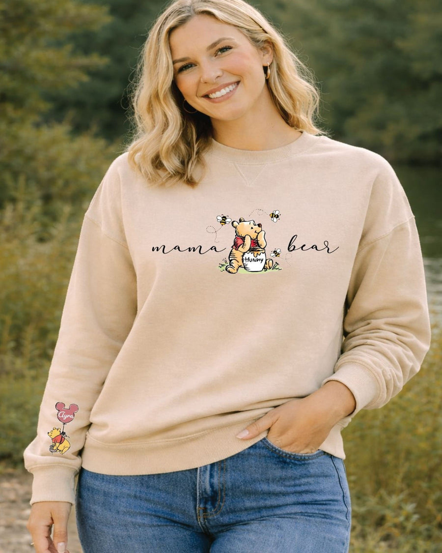 A smiling woman wearing a beige sweatshirt with a Winnie the Pooh graphic and the text "mama bear" printed on it.
