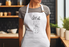A woman wearing a white apron with the text "Oh Allah, Bless this mess" printed on it.