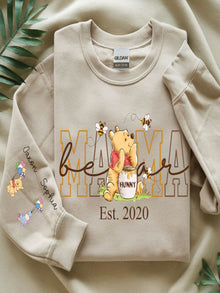A beige sweatshirt with a Winnie the Pooh-themed design, featuring the character Winnie the Pooh and the text "Mama HUNNY" along with the year "Est. 2020".
