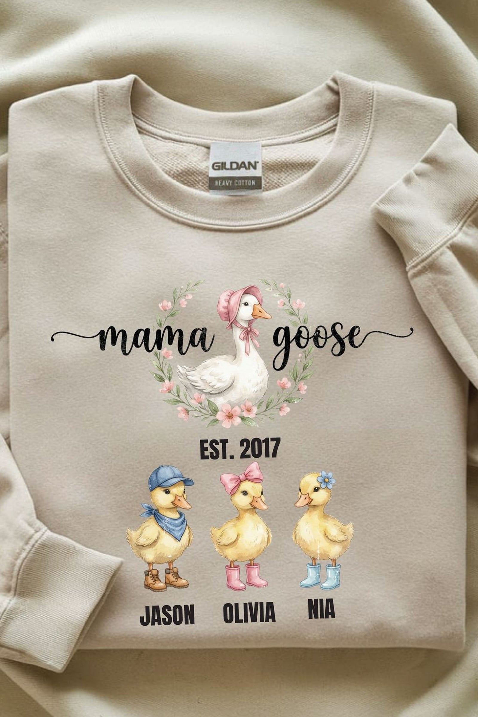 A beige sweatshirt with a graphic design featuring three cartoon ducks and the text "mama goose" above them.