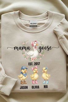 A beige sweatshirt with a graphic design featuring three cartoon ducks and the text "mama goose" above them.