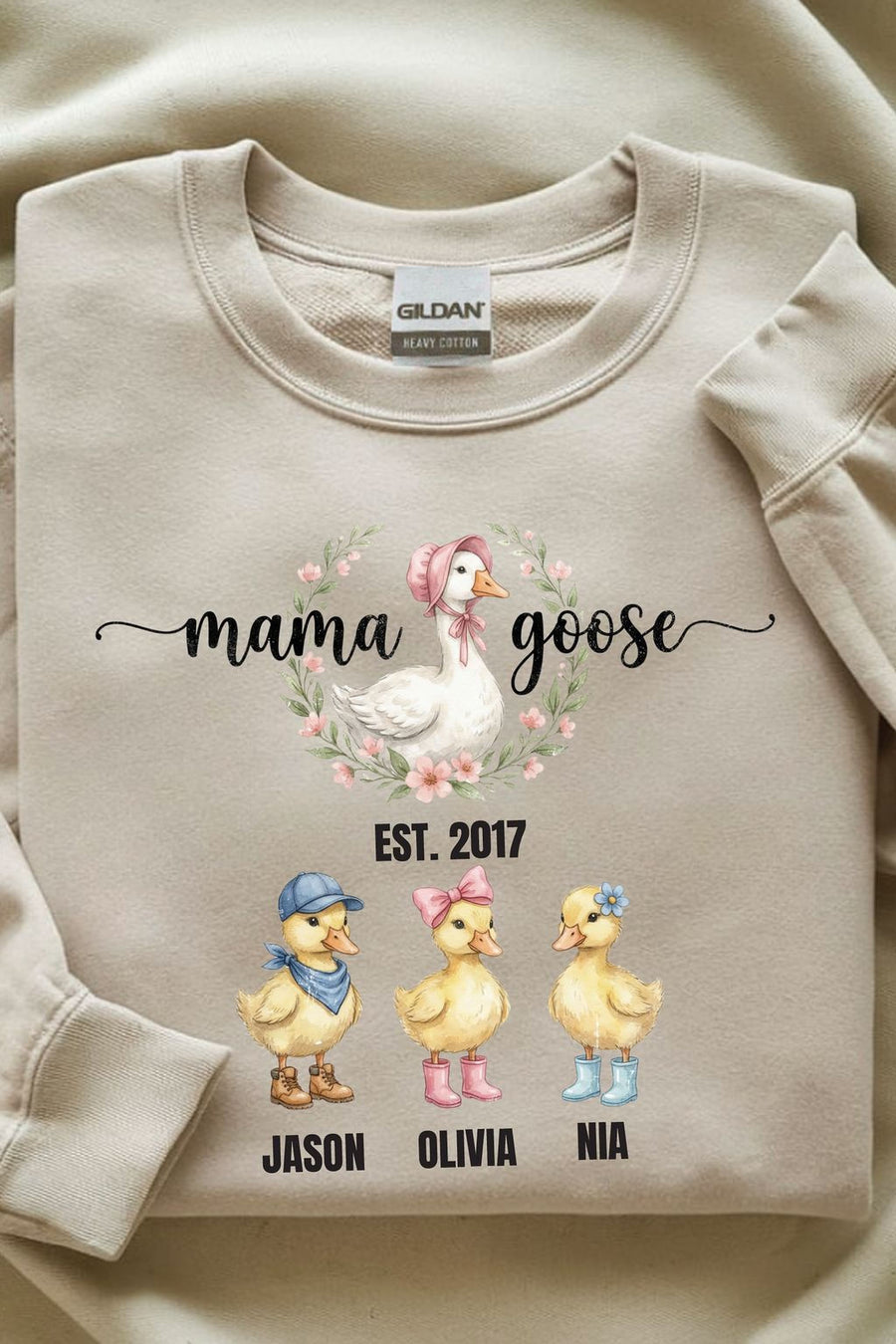 A beige sweatshirt with a graphic design featuring three cartoon ducks and the text "mama goose" above them.