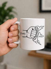 White personalized dad mug featuring custom family fist bump line art and children’s names held in hand indoors.