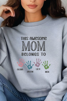 A woman wearing a gray sweatshirt with a message that says "This awesome mom belongs to Olivia, Jason, Lily, and Nick".