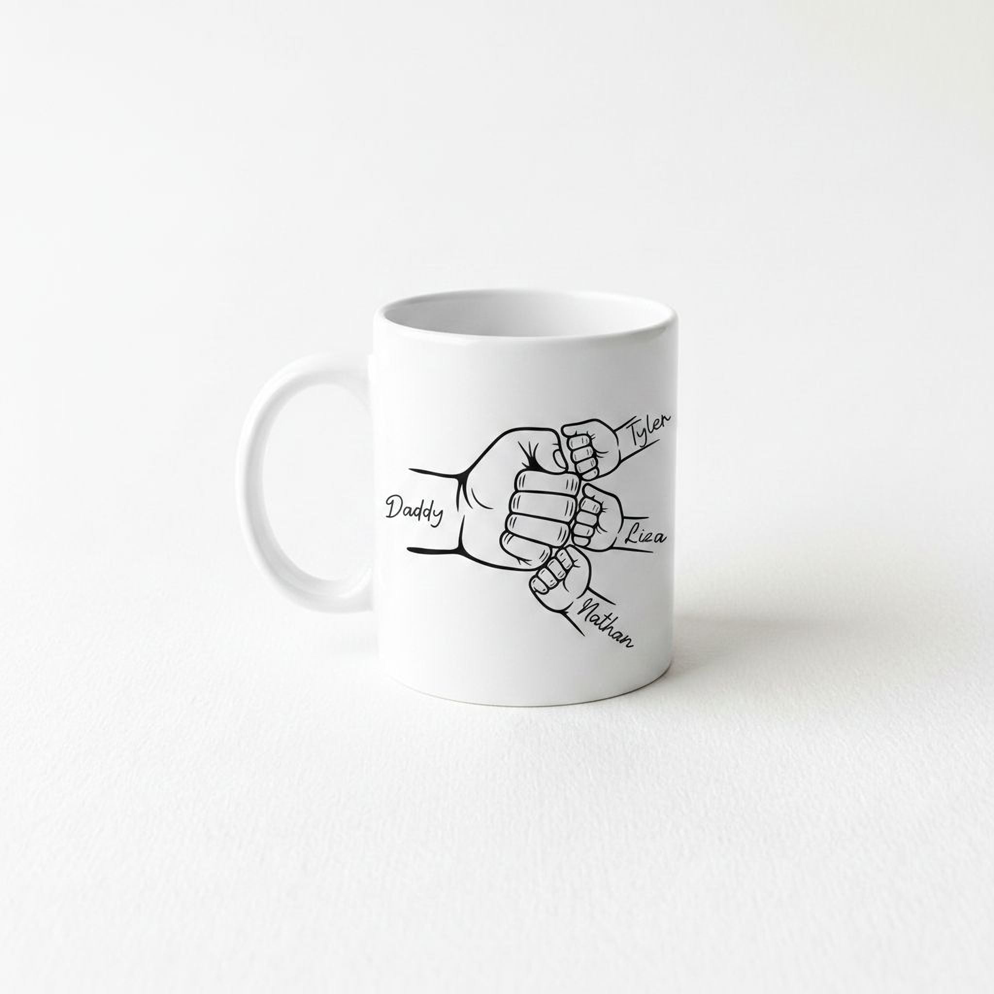 A white ceramic mug with a black and white illustration of two hands, one larger and one smaller, connected by a fist. The text "Daddy, Tyler, Liza, Nathan" is written above the illustration.