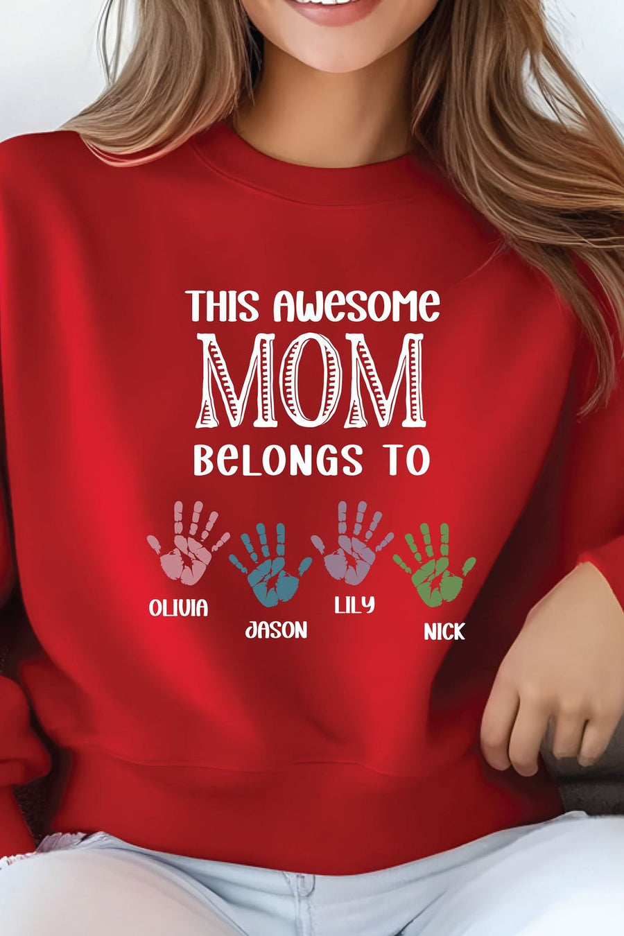 A woman wearing a red sweater with the text "This awesome MOM belongs to" printed on it, along with handprints of three different individuals.