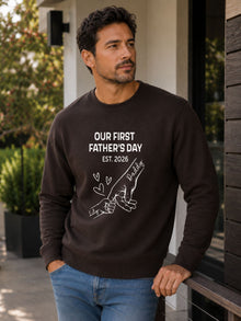 sweatshirt featuring personalized Our First Father’s Day design with minimalist daddy and baby hand outline artwork worn by male model outdoors.