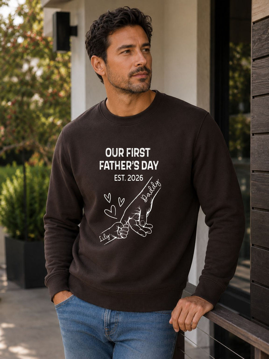 sweatshirt featuring personalized Our First Father’s Day design with minimalist daddy and baby hand outline artwork worn by male model outdoors.