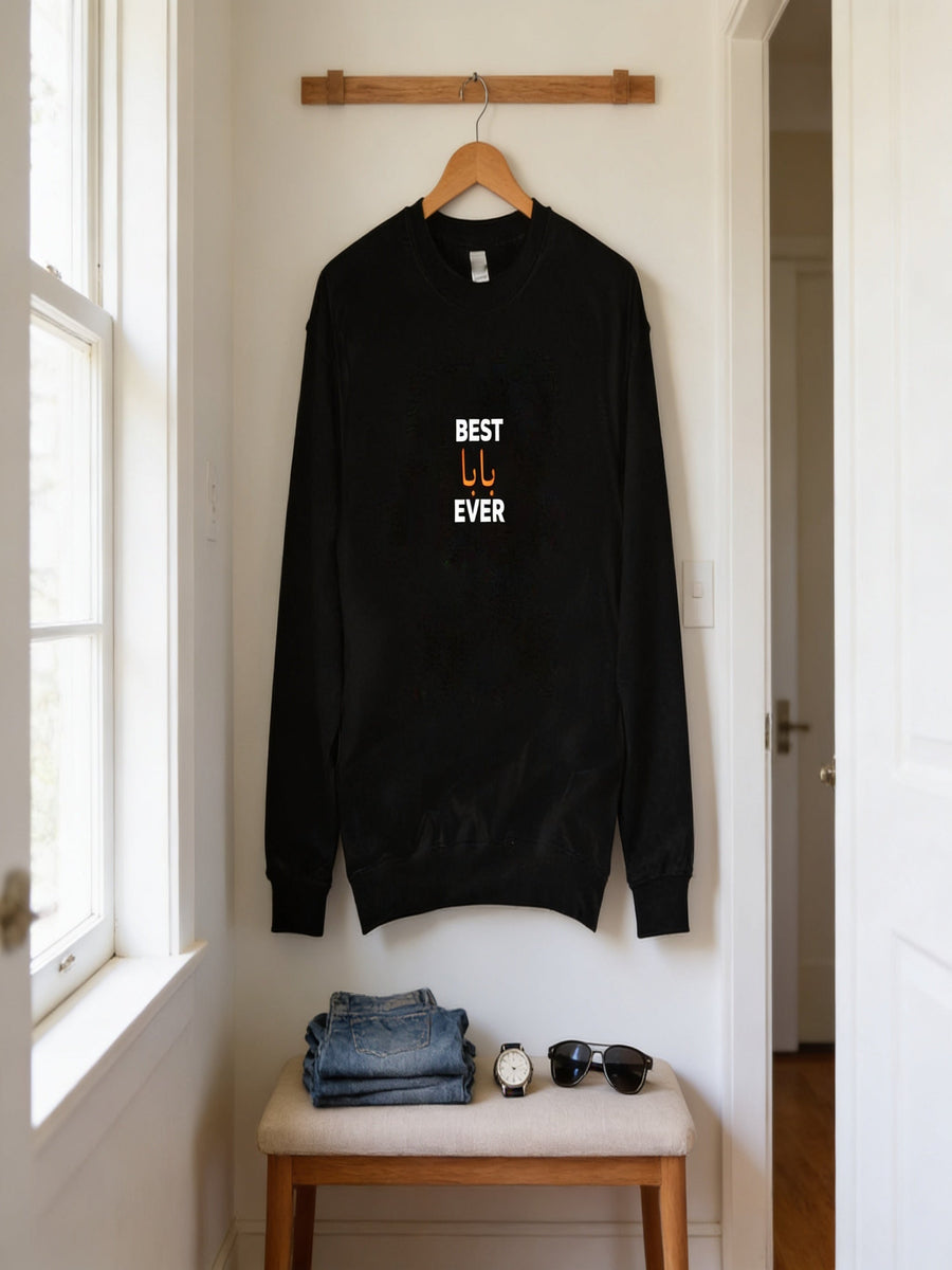 A black sweatshirt with the text "BEST U EVER" printed on it is hanging on a wooden hanger on a wall. Below the sweatshirt, there is a folded pair of jeans and a pair of sunglasses.