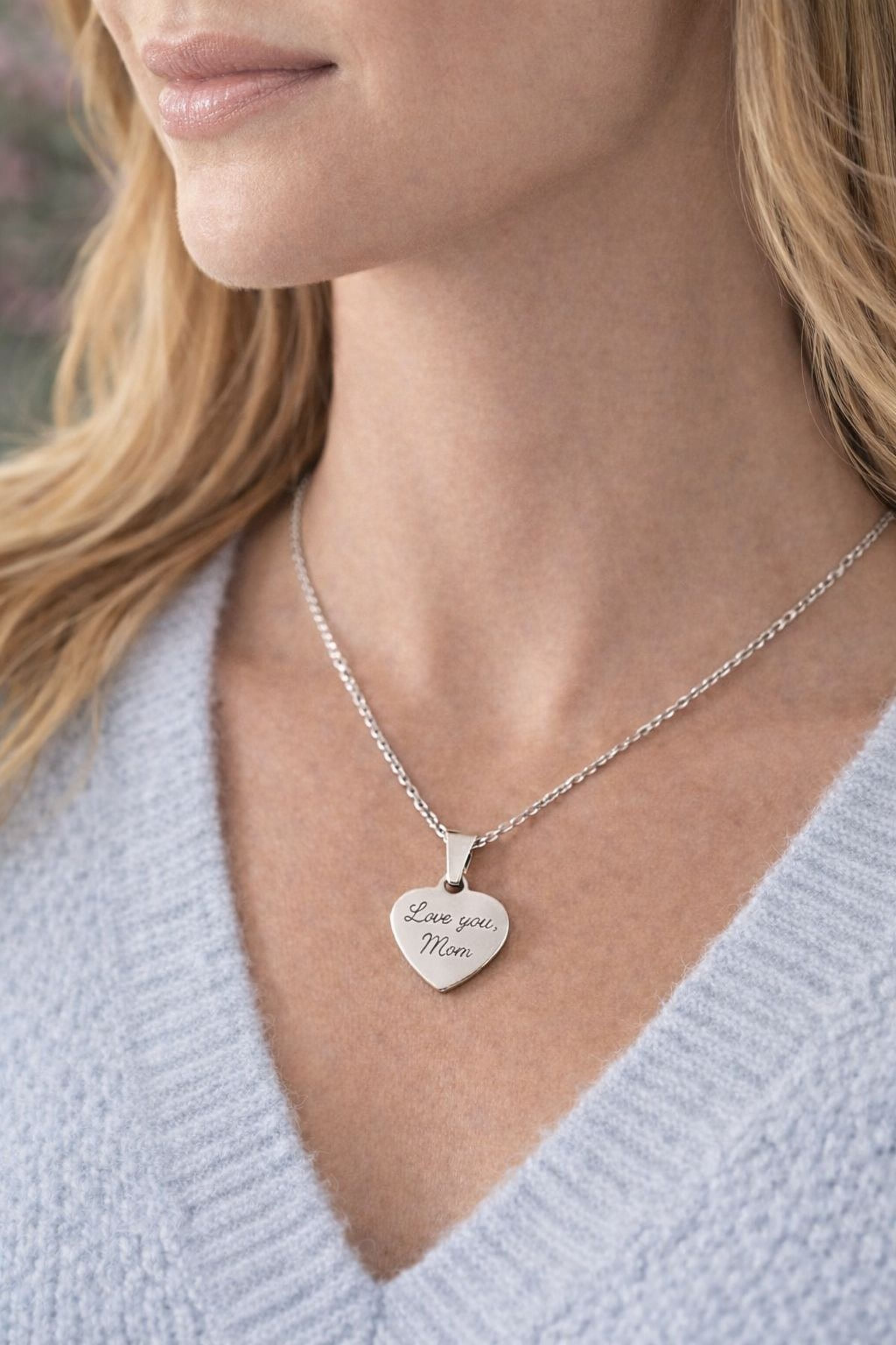 A woman wearing a silver necklace with a heart-shaped pendant that says "Love you Mom".