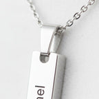 A close-up view of a silver necklace pendant with the name "Emil" engraved on it.