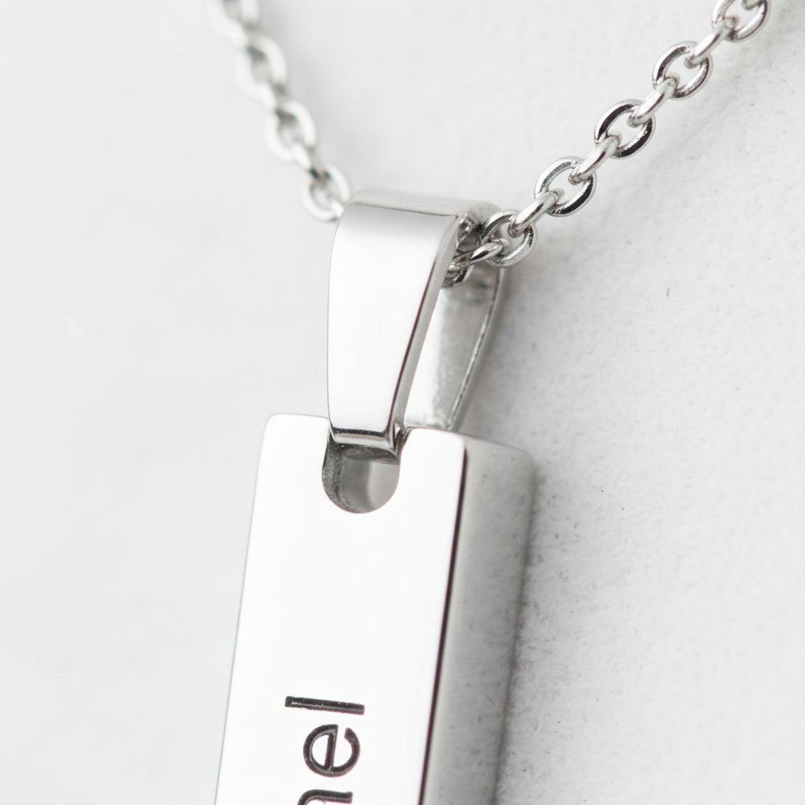 A close-up view of a silver necklace pendant with the name "Emil" engraved on it.