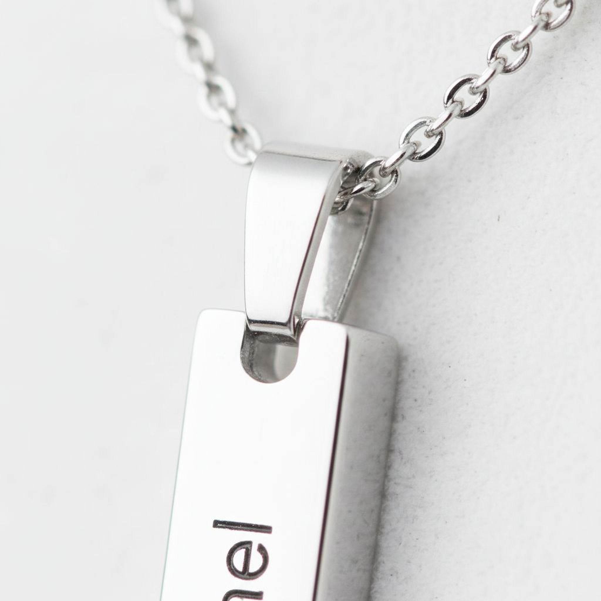 A close-up view of a silver necklace pendant with the name "Emil" engraved on it.