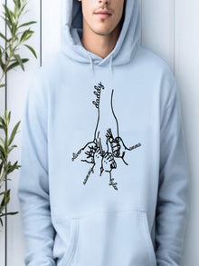 A person wearing a light blue hoodie with a black graphic design depicting a hand holding a family tree with the names of family members.