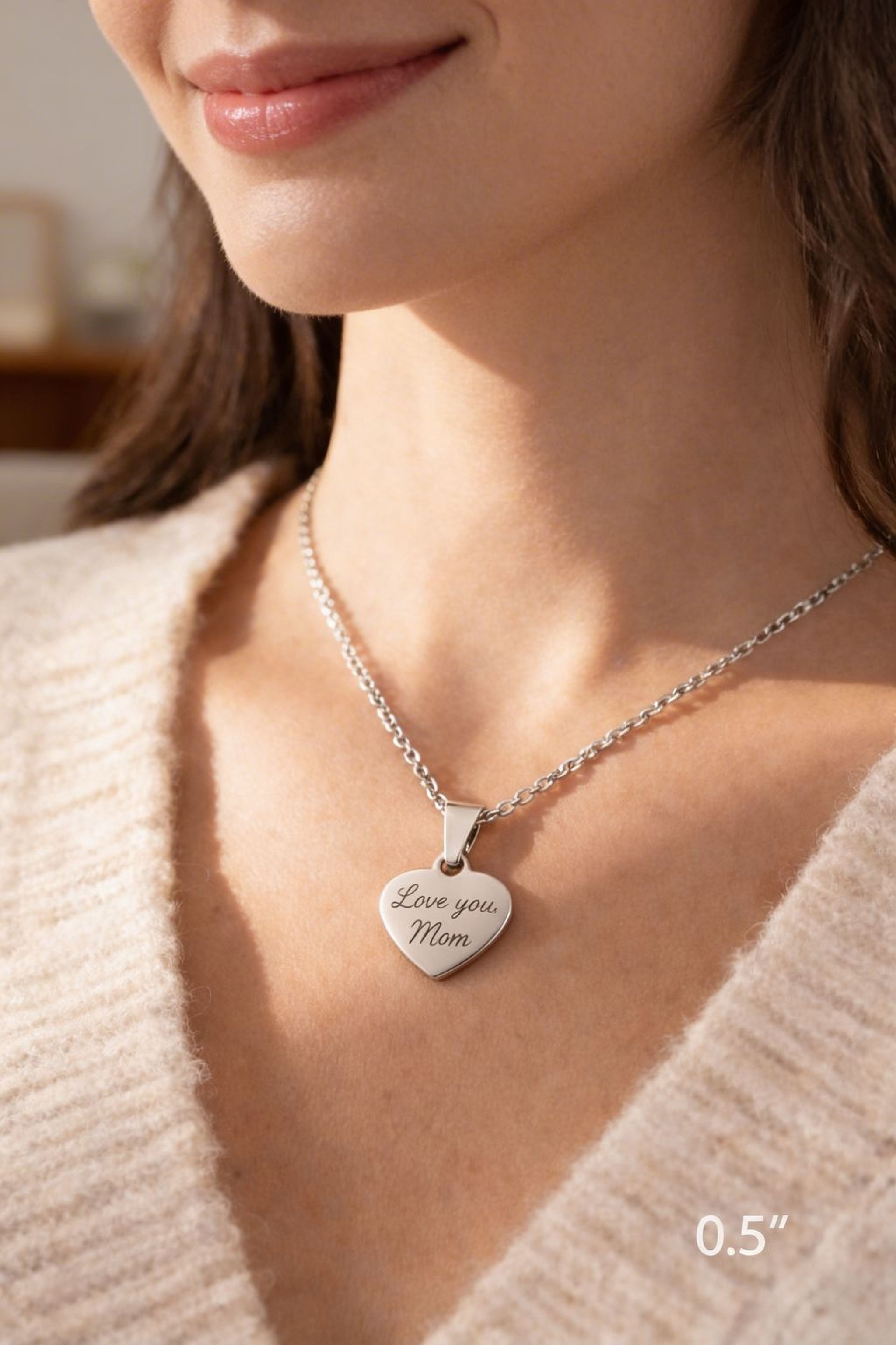 A woman wearing a silver necklace with a heart-shaped pendant engraved with the message "Love you Mom".