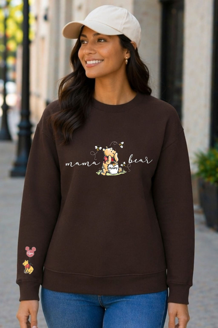 A woman wearing a brown sweatshirt with a Winnie the Pooh graphic and the text "mama bear" printed on it, smiling and looking to the side.
