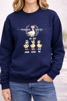 A woman wearing a navy blue sweatshirt with a graphic design featuring three cartoon ducks and the text "Mama Goose" above them.