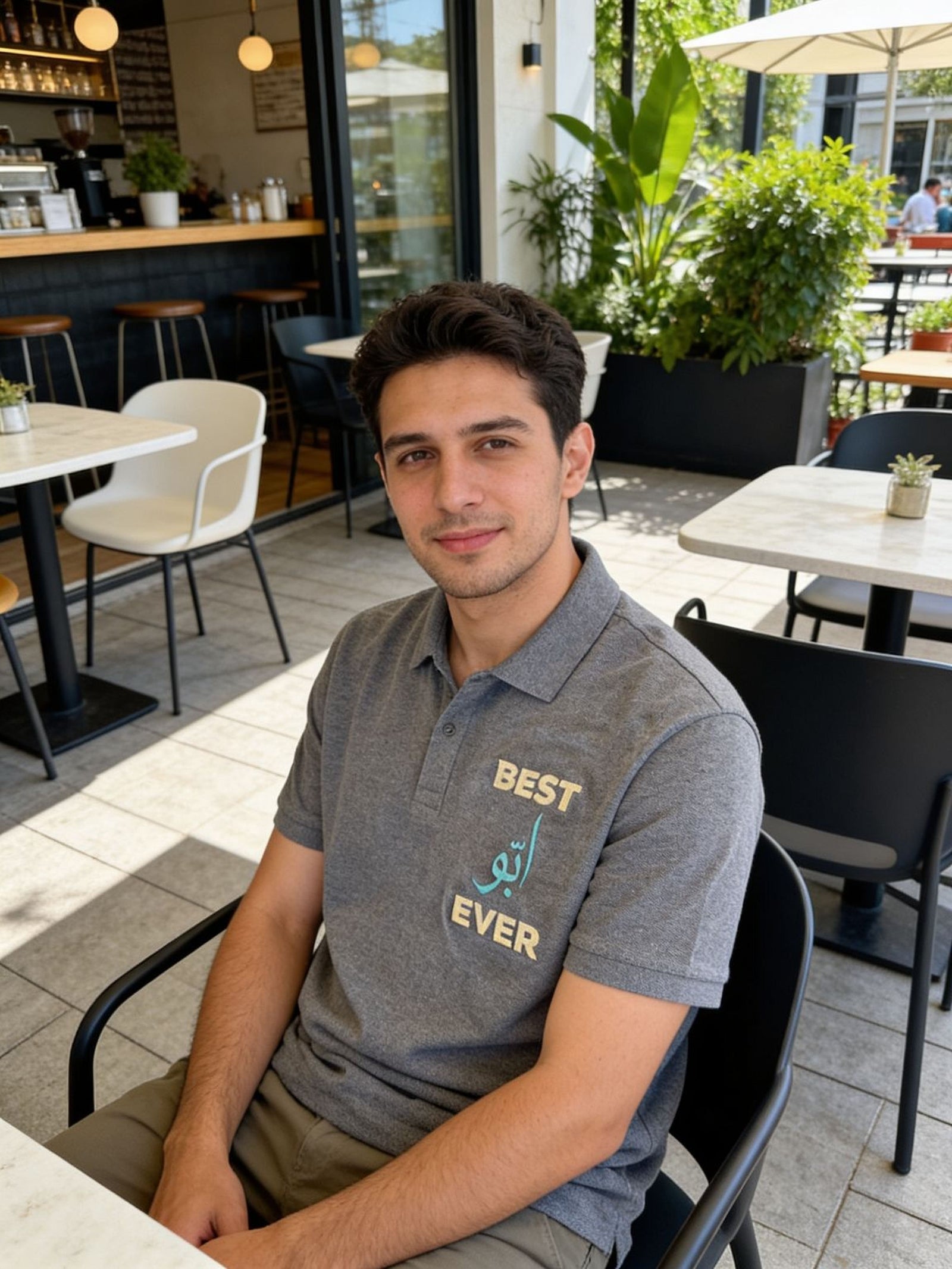 A young man wearing a grey polo shirt with the text "BEST EVER" is sitting at a table in a restaurant.