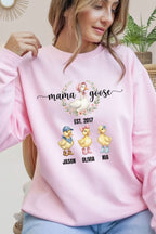 A woman wearing a pink sweatshirt with a graphic design featuring three cartoon ducks and the text "mama goose" and "Est. 2017 Jason Olivia Nia".