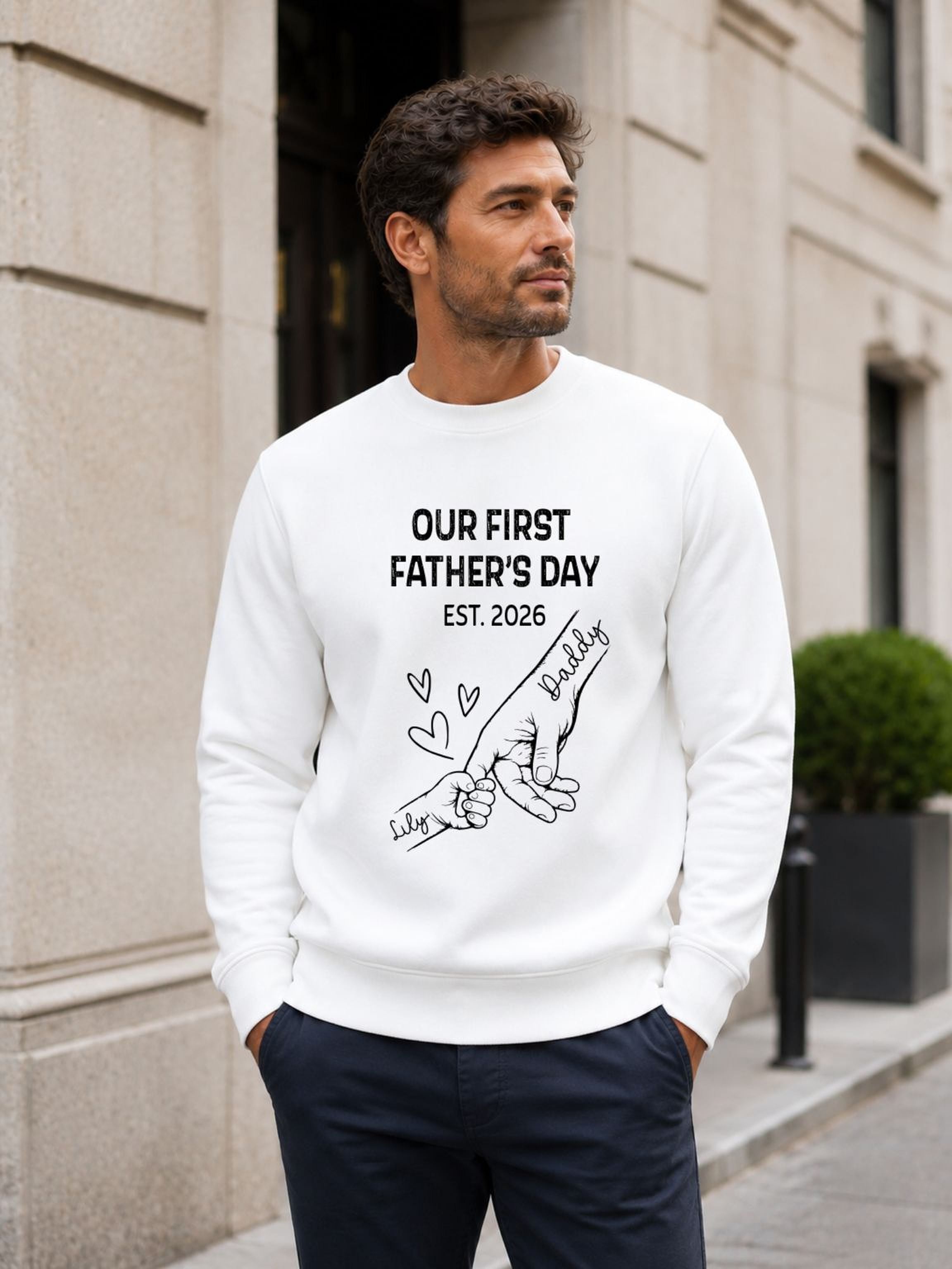 sweatshirt featuring personalized Our First Father’s Day design with minimalist daddy and baby hand outline artwork worn by male model outdoors.
