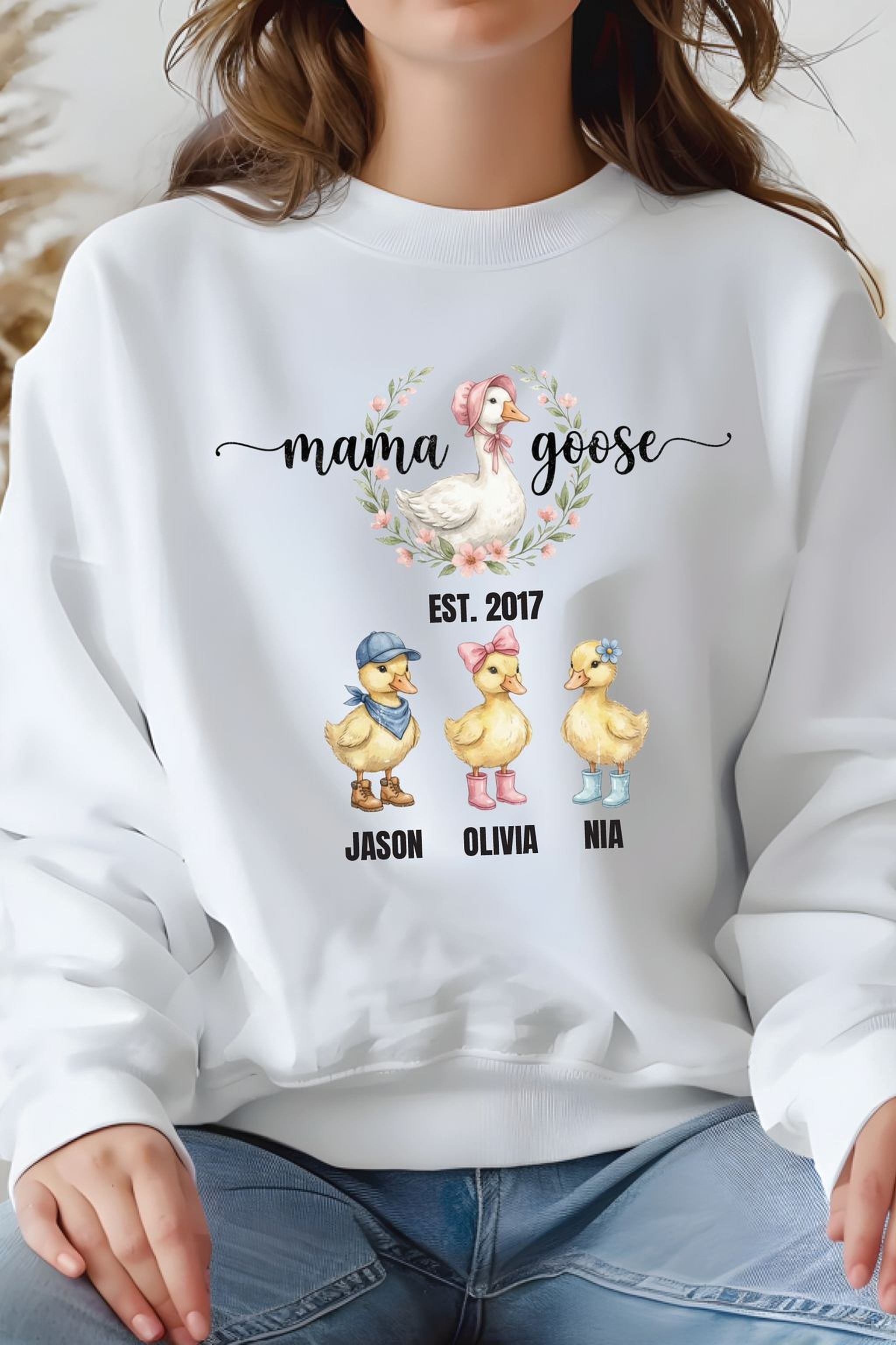 A white sweatshirt with a graphic design featuring three cartoon ducks and the text "mama goose" above them.