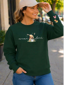 A woman wearing a green sweatshirt with a Winnie the Pooh logo and the text "mama bear" printed on it, smiling and looking to the side.