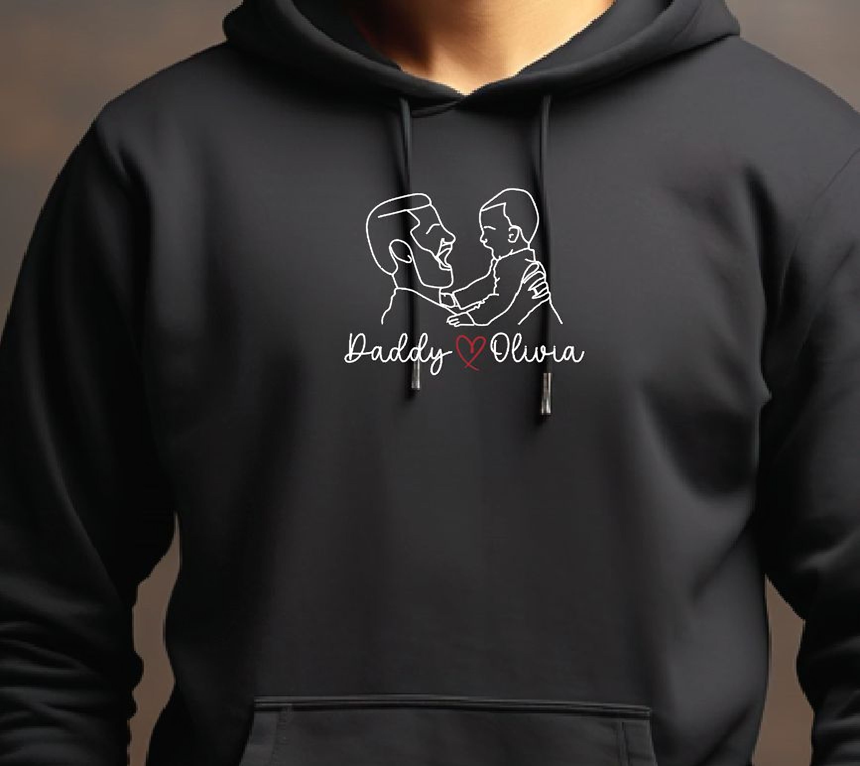 A black hoodie with a graphic design on the front, depicting two people embracing. The text below the design reads "Daddy & Olivia".