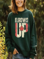 A woman wearing a green sweatshirt with the text "ELBOWS UP" printed on it, along with a red maple leaf.