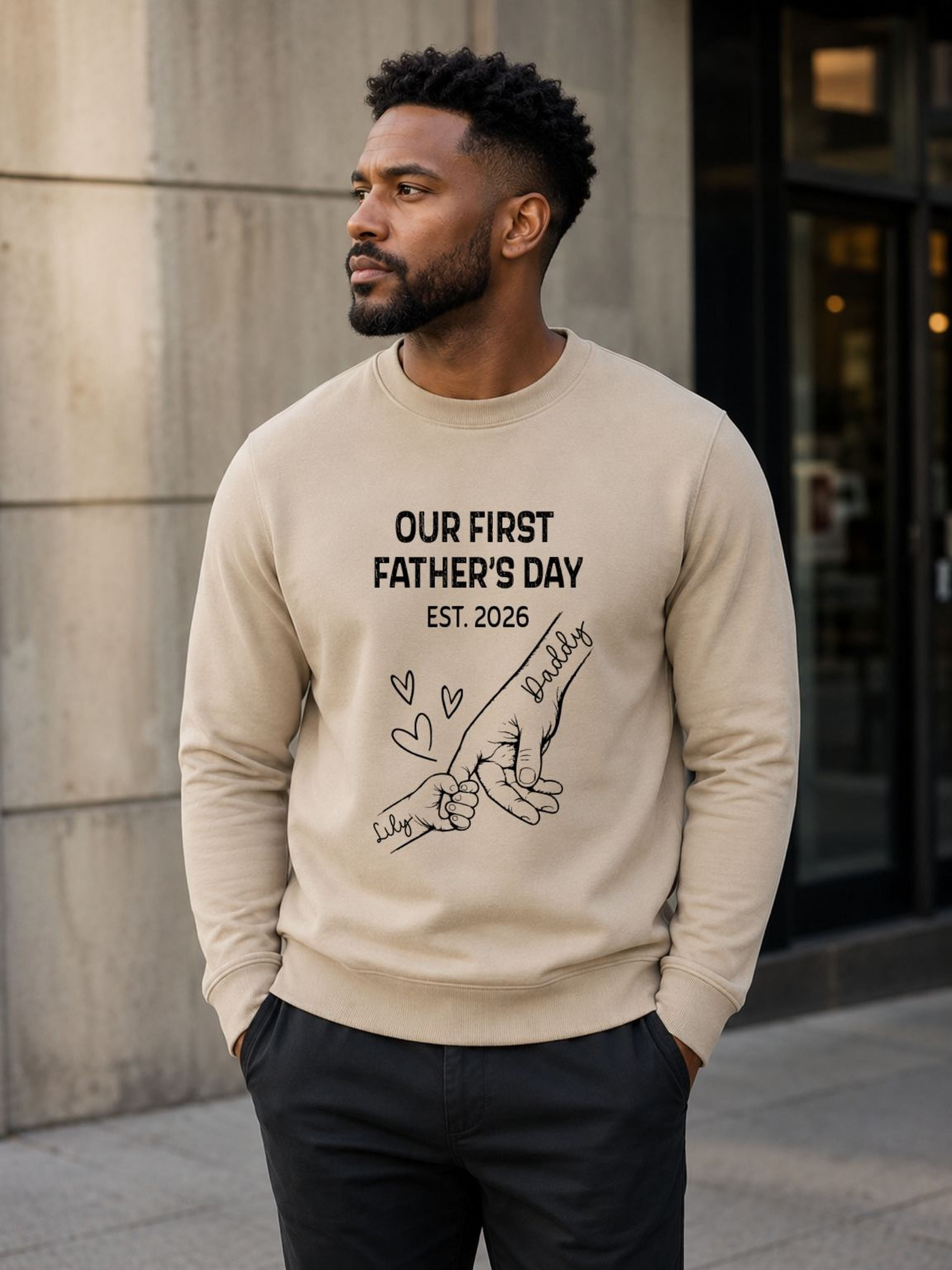 sweatshirt featuring personalized Our First Father’s Day design with minimalist daddy and baby hand outline artwork worn by male model outdoors.