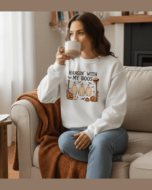 Woman wearing white Halloween sweatshirt with 'Hangin With My Boos' ghost graphic and pumpkins