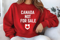 A person wearing a red sweatshirt with the text "CANADA NOT FOR SALE" printed on it.