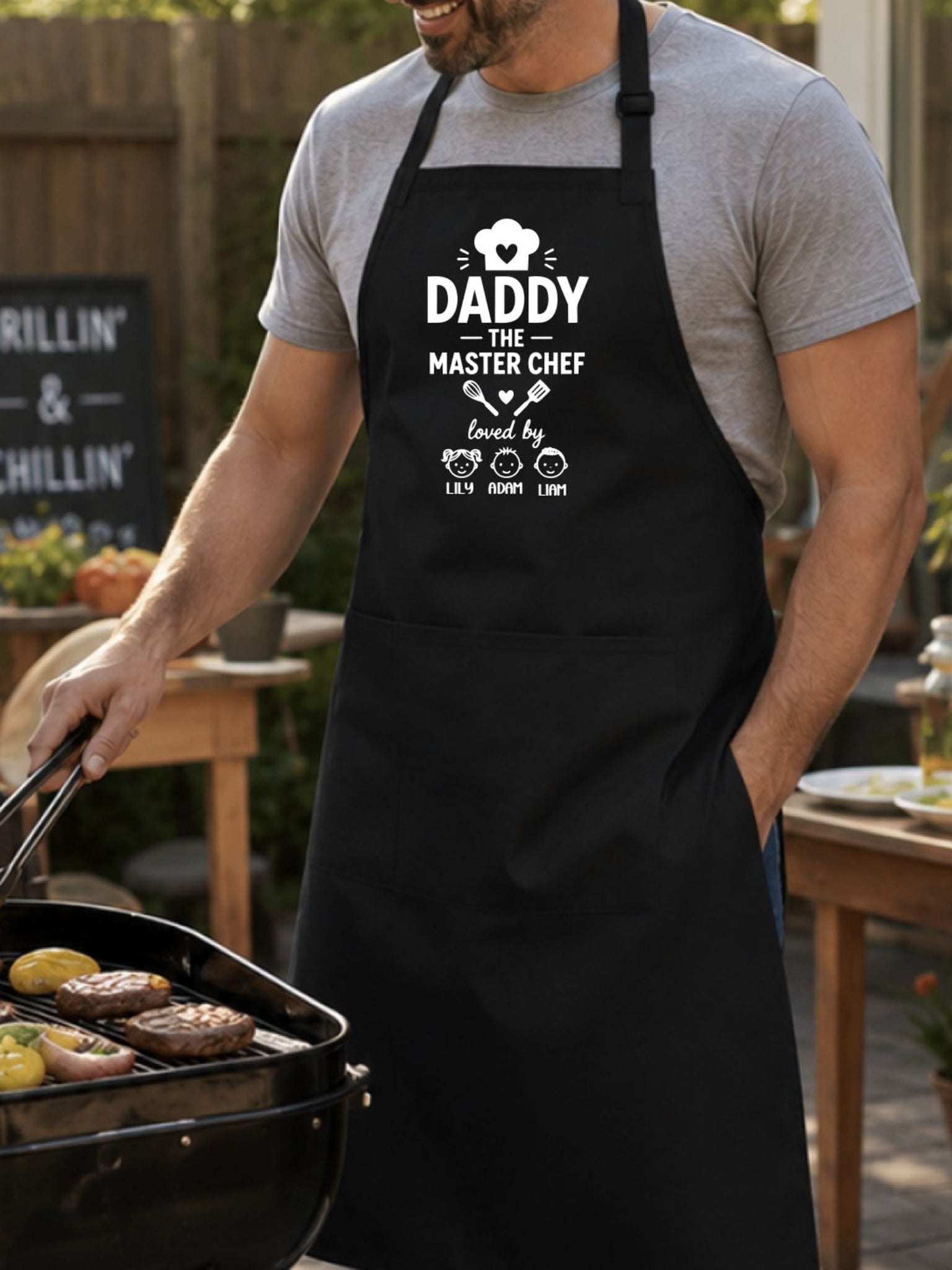 personalized Daddy The Master Chef BBQ apron with custom kids names worn by dad grilling outdoors.