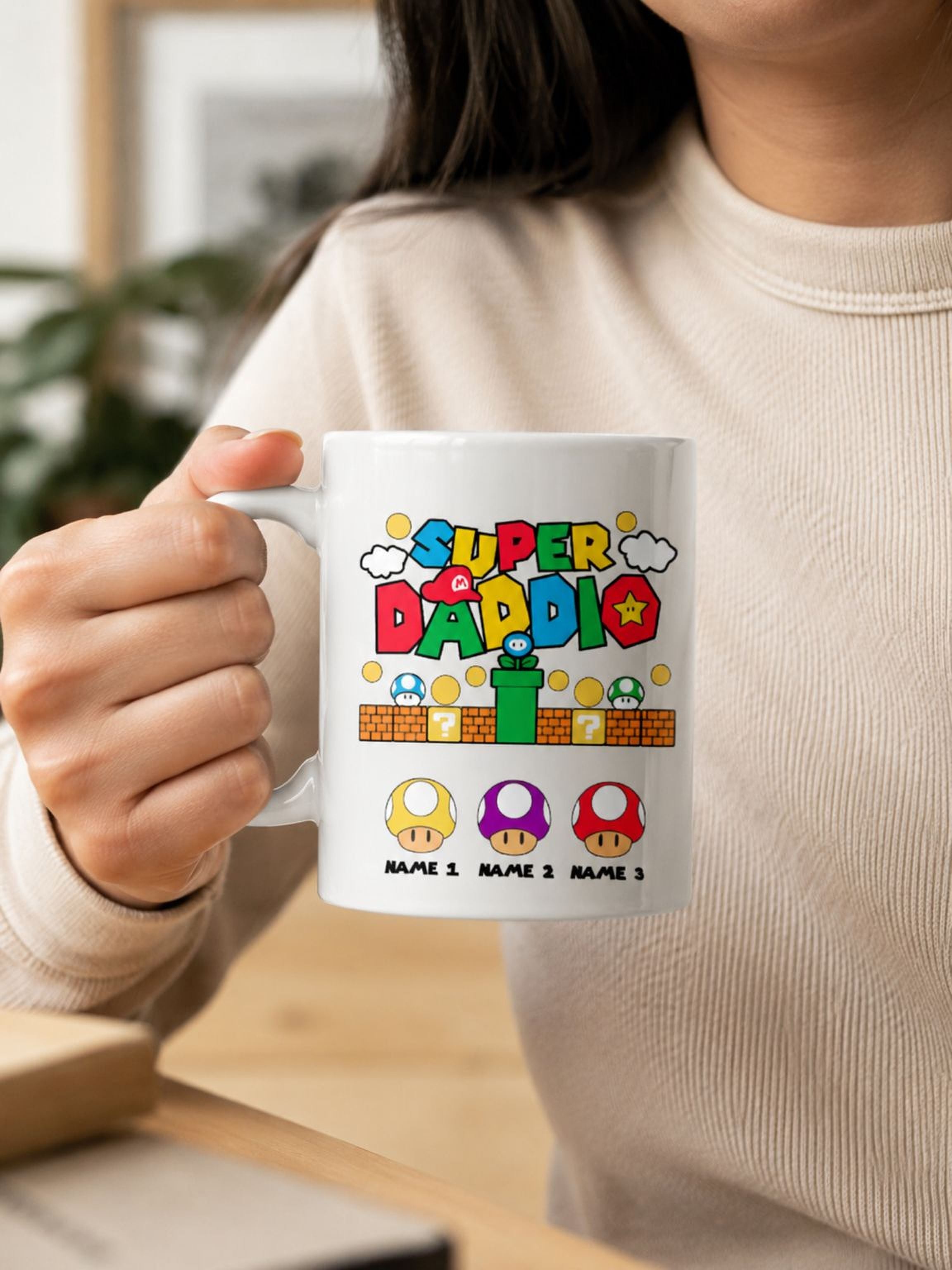 White Super Daddio personalized coffee mug with retro gamer-inspired colorful design and custom kids names held by person indoors.