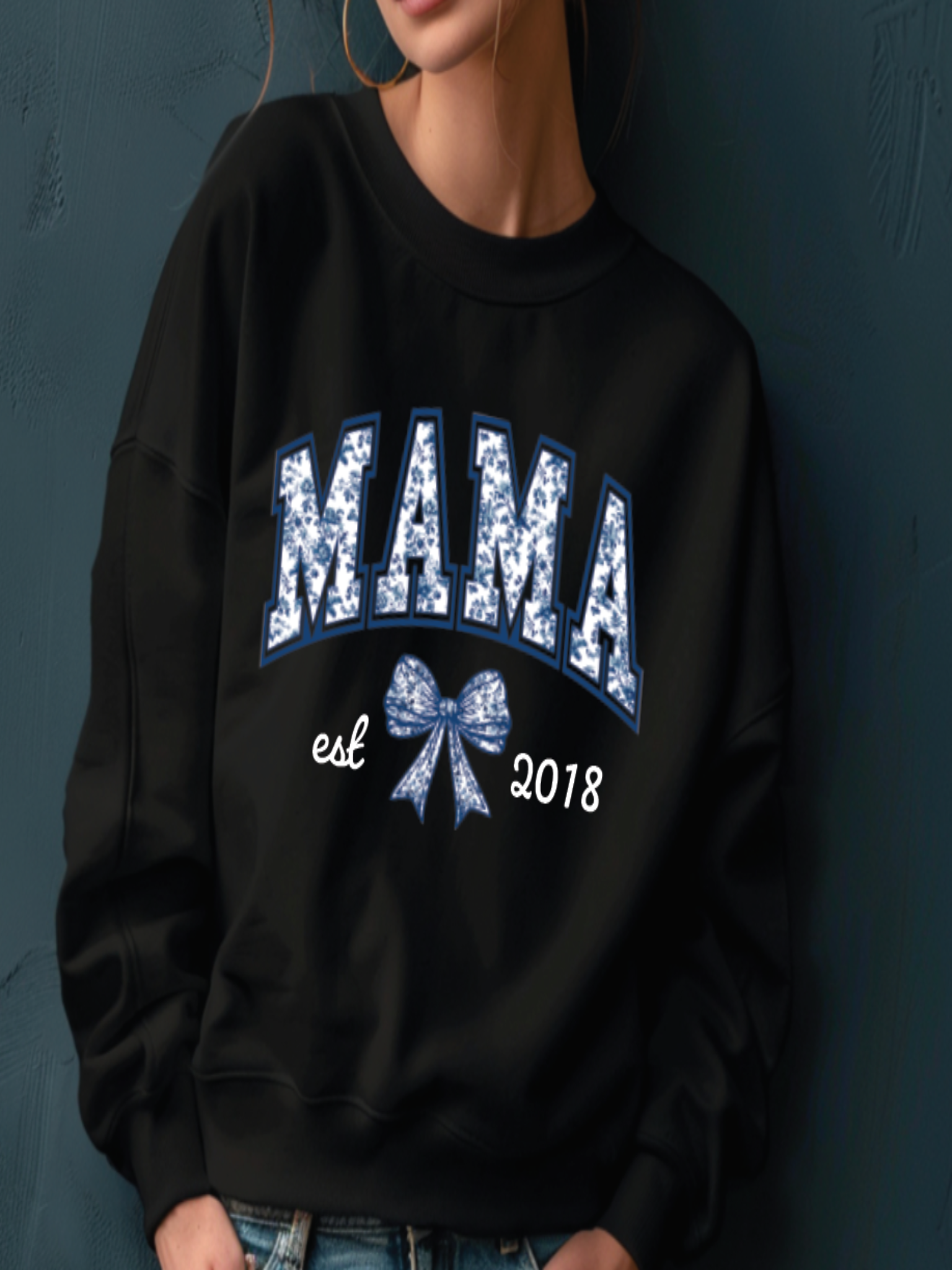 Black sweatshirt with 'MAMA est 2018' text and blue bow design on a dark background