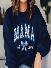Person wearing a navy blue sweatshirt with 'MAMA est 2018' text and bow design.