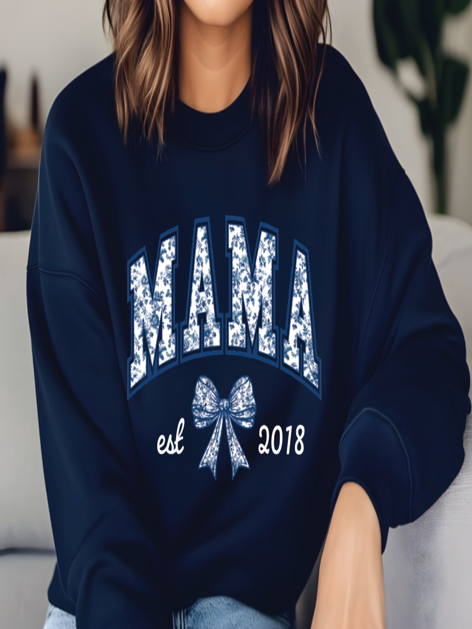 Person wearing a navy blue sweatshirt with 'MAMA est 2018' text and bow design.