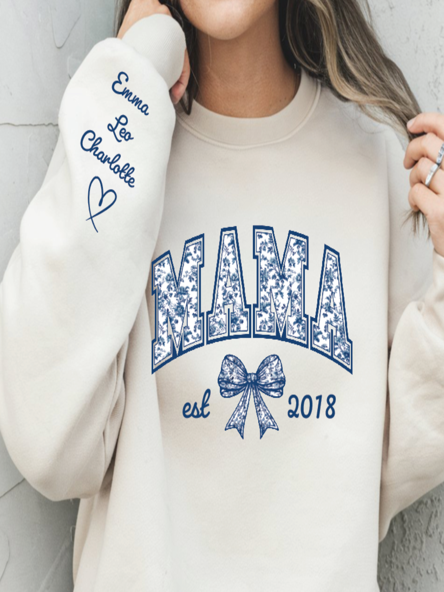 Beige sweatshirt with 'MAMA est 2018' design and personalized text on sleeve.