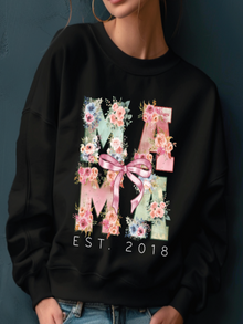 Black sweatshirt with floral 'MAMA' design and 'EST. 2018' text on a dark background