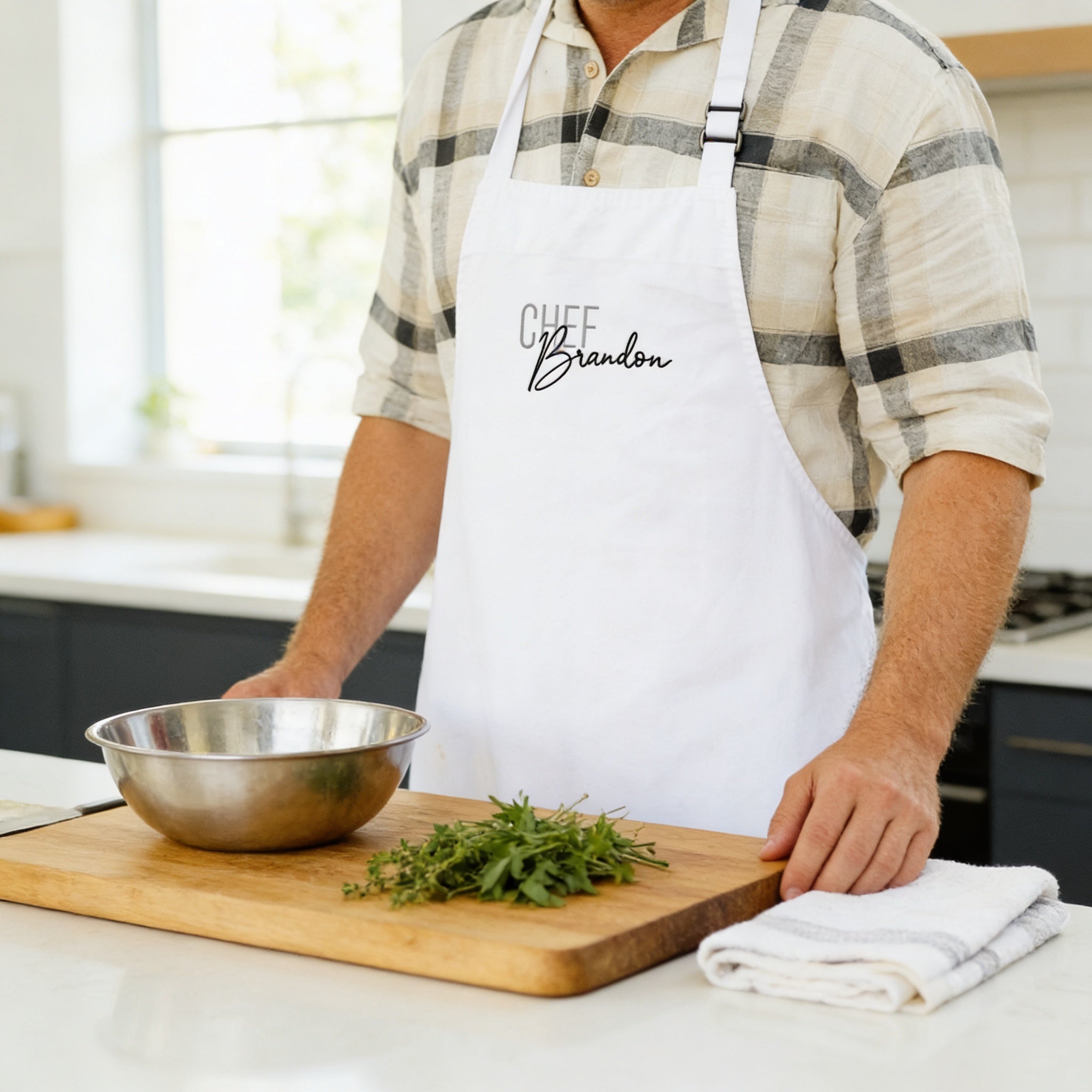 A man wearing a white apron with the name "Chef Brandon" is standing in a kitchen, preparing food on a wooden cutting board.