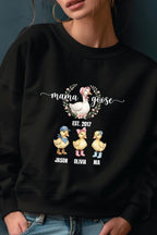 A woman wearing a black sweatshirt with a graphic design featuring three cartoon ducks and the text "mama goose" above them.