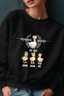 A woman wearing a black sweatshirt with a graphic design featuring three cartoon ducks and the text "mama goose" above them.