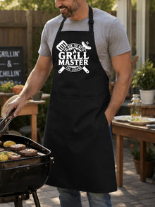 A man wearing a black apron with a white graphic design is grilling food outdoors.
